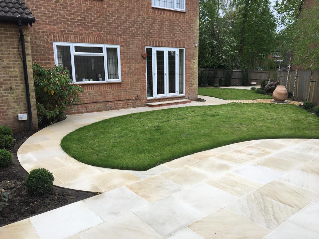 Buff sandstone curved patio with new turf lawn at rear brick house, Surrey