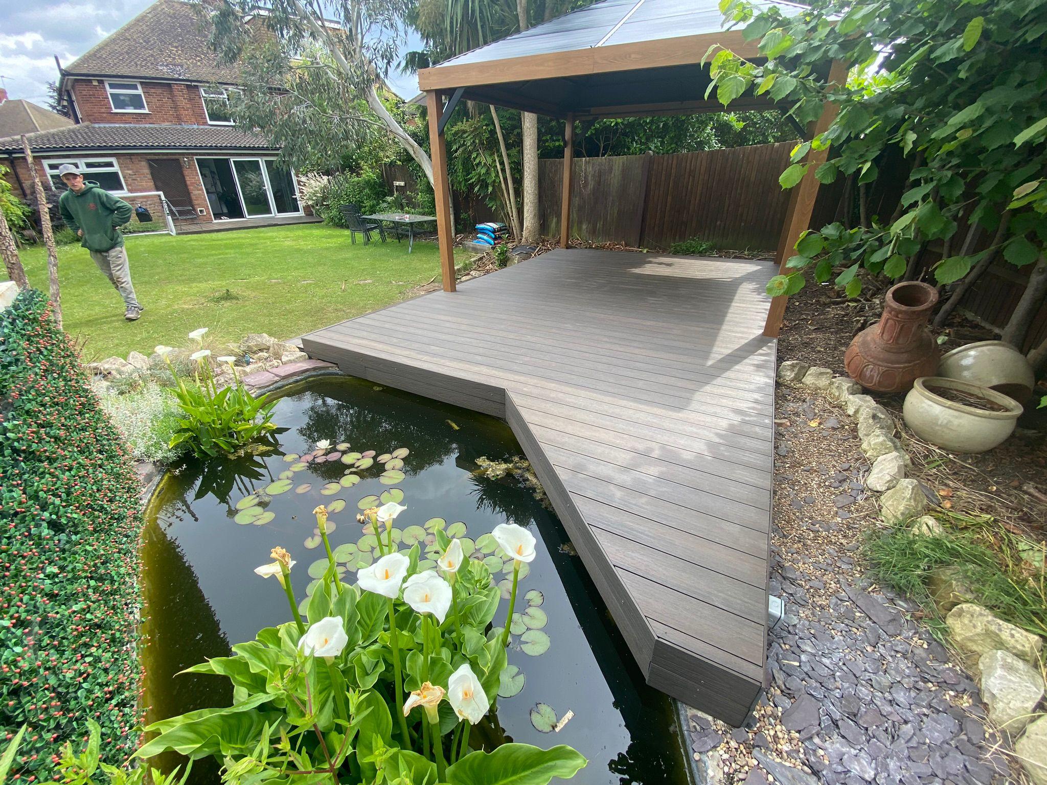Composite decking with gazebo structure beside garden pond, Surrey