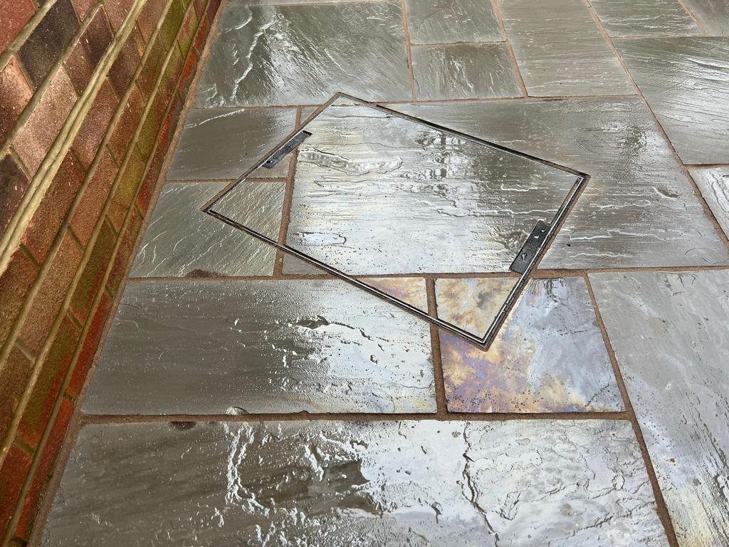 Dark slate patio close-up with stainless steel manhole cover, Surrey
