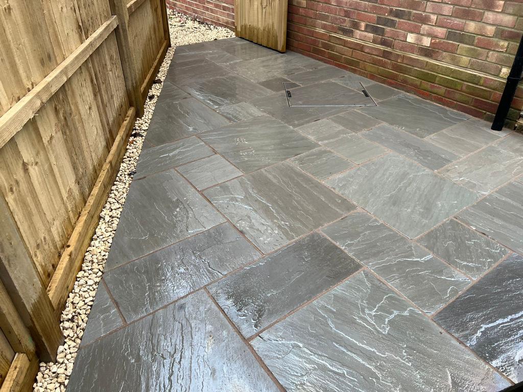 Dark slate patio side return with gravel border and close-board fence, Surrey