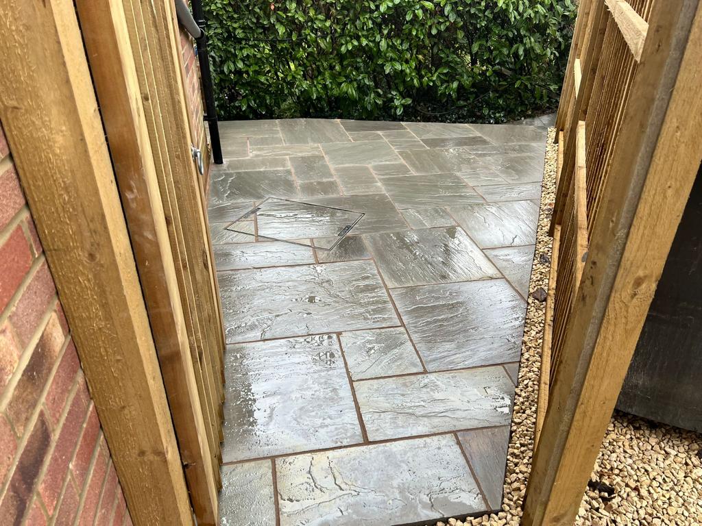 Dark slate patio viewed through timber gate with gravel border, Surrey