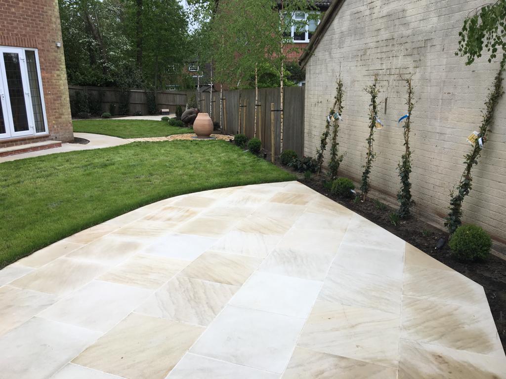 Large buff sandstone patio with curved lawn and climbing plants, Surrey